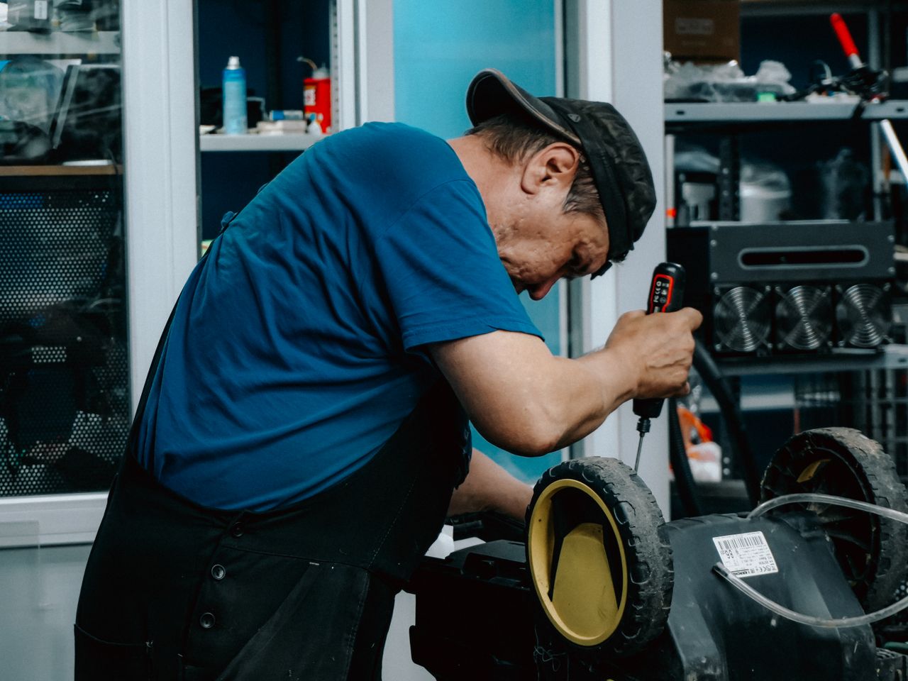 Focused adult male is repairing an electric toy vehicle in a workshop setting.